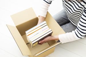 Person placing books into a cardboard box wearing a striped shirt and jeans visible from an overhead angle