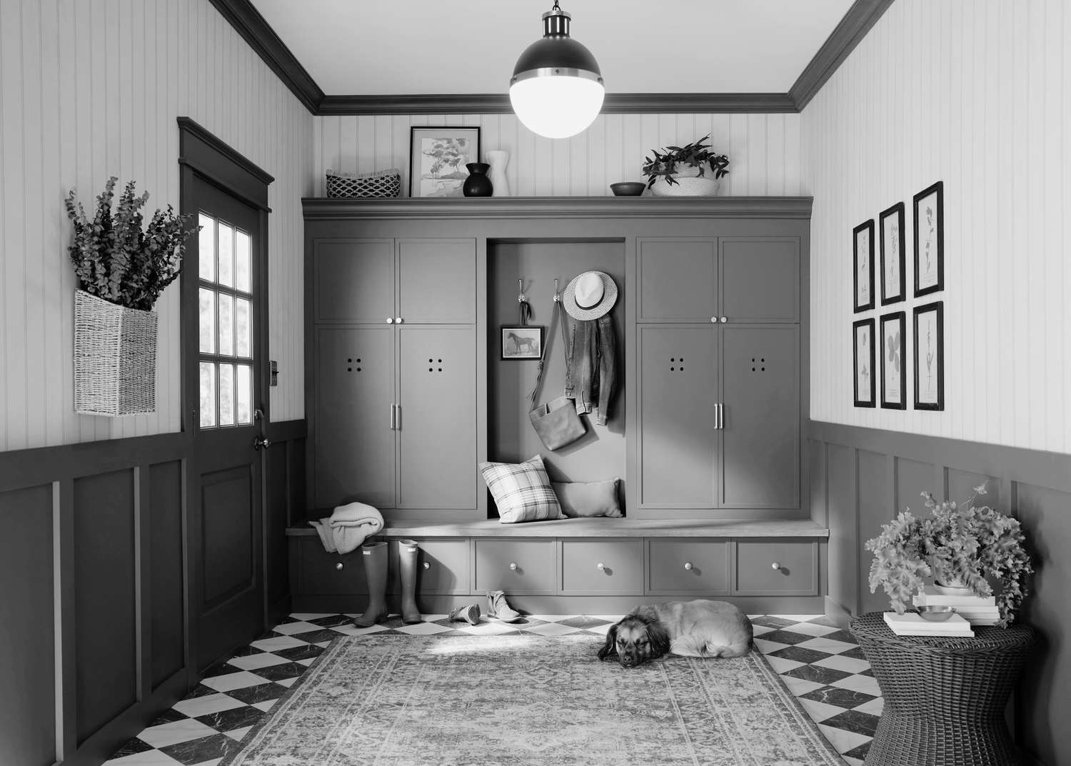 A mudroom with builtin storage cabinets coat hooks a bench and decorative touches such as plants and framed artwork