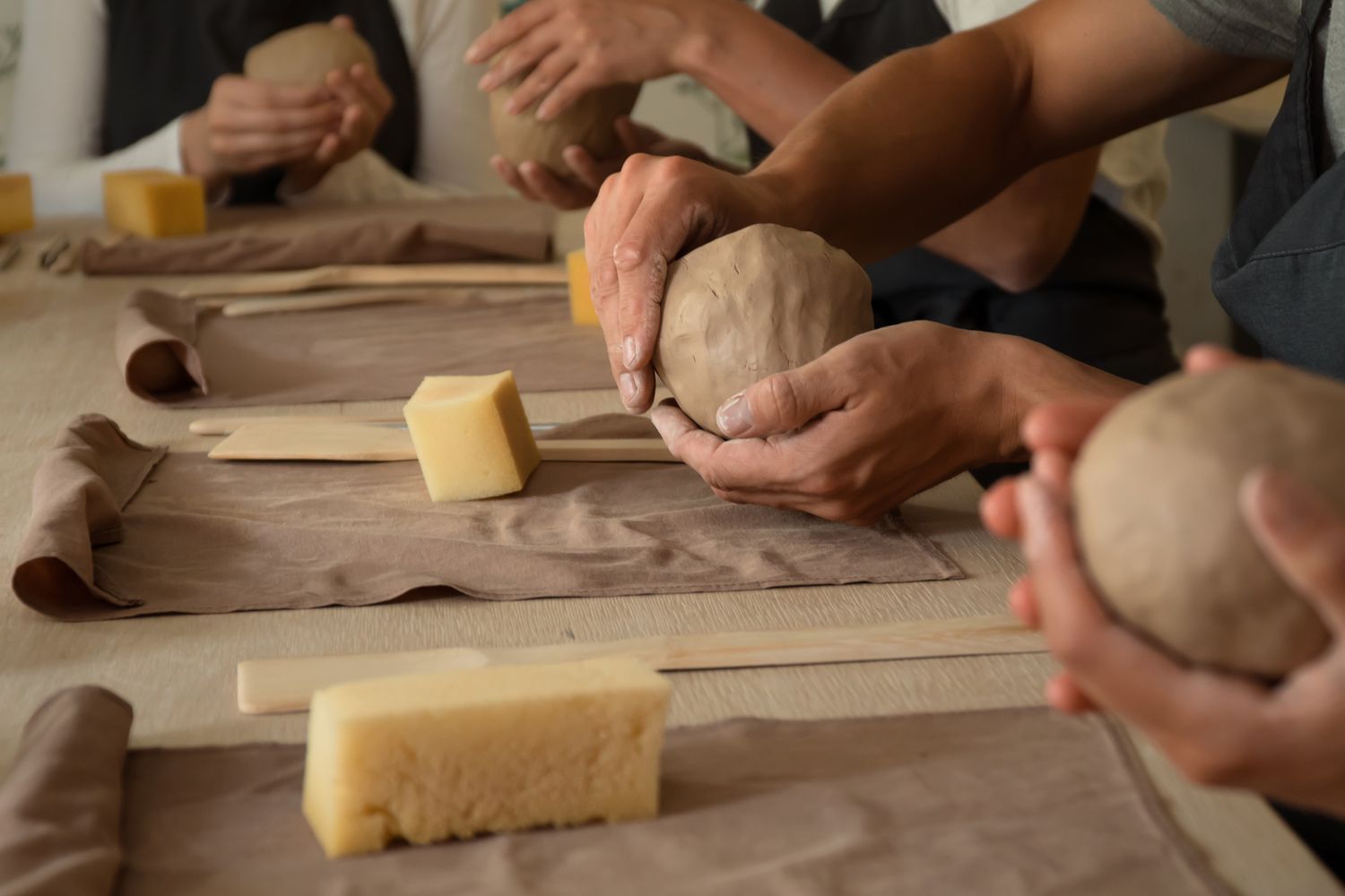 Hands shaping clay on a table, with materials and tools for pottery