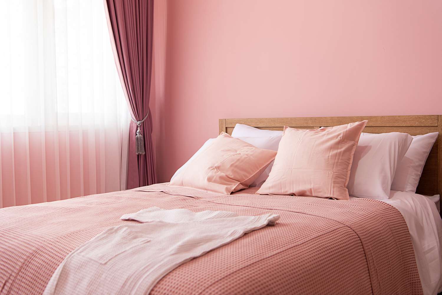 A neatly made bed with pillows and a throw blanket positioned next to a window with curtains