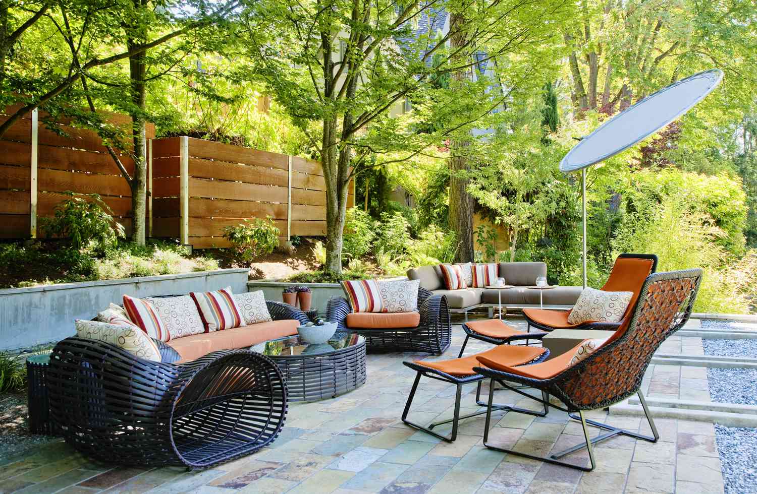 Outdoor patio area with modern furniture and cushions surrounded by trees and greenery