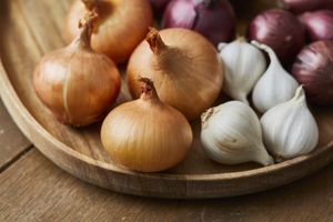 A wooden platter with onions garlic and shallots arranged together