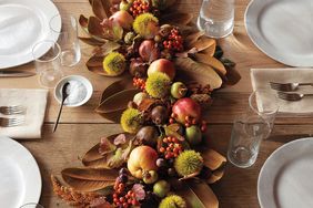 Thanksgiving table centerpiece featuring fruit foliage and decorations with table setting in view