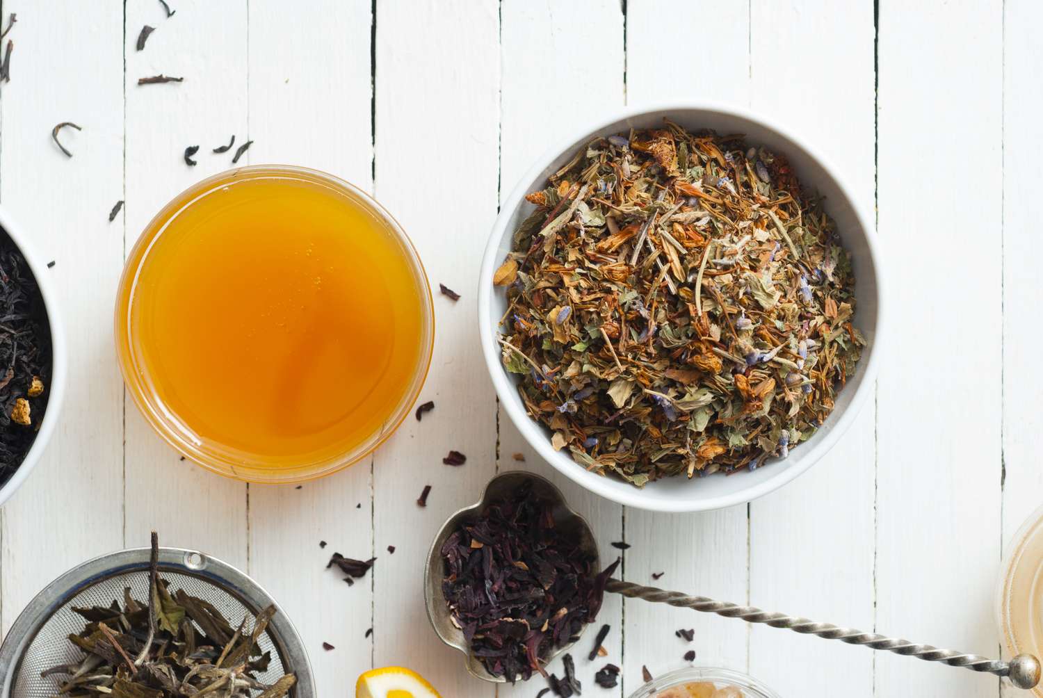 Dried herbal tea ingredients and a glass of prepared tea on a white wooden surface