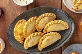 A serving plate with six empanadas placed on a table, side dishes partially visible around