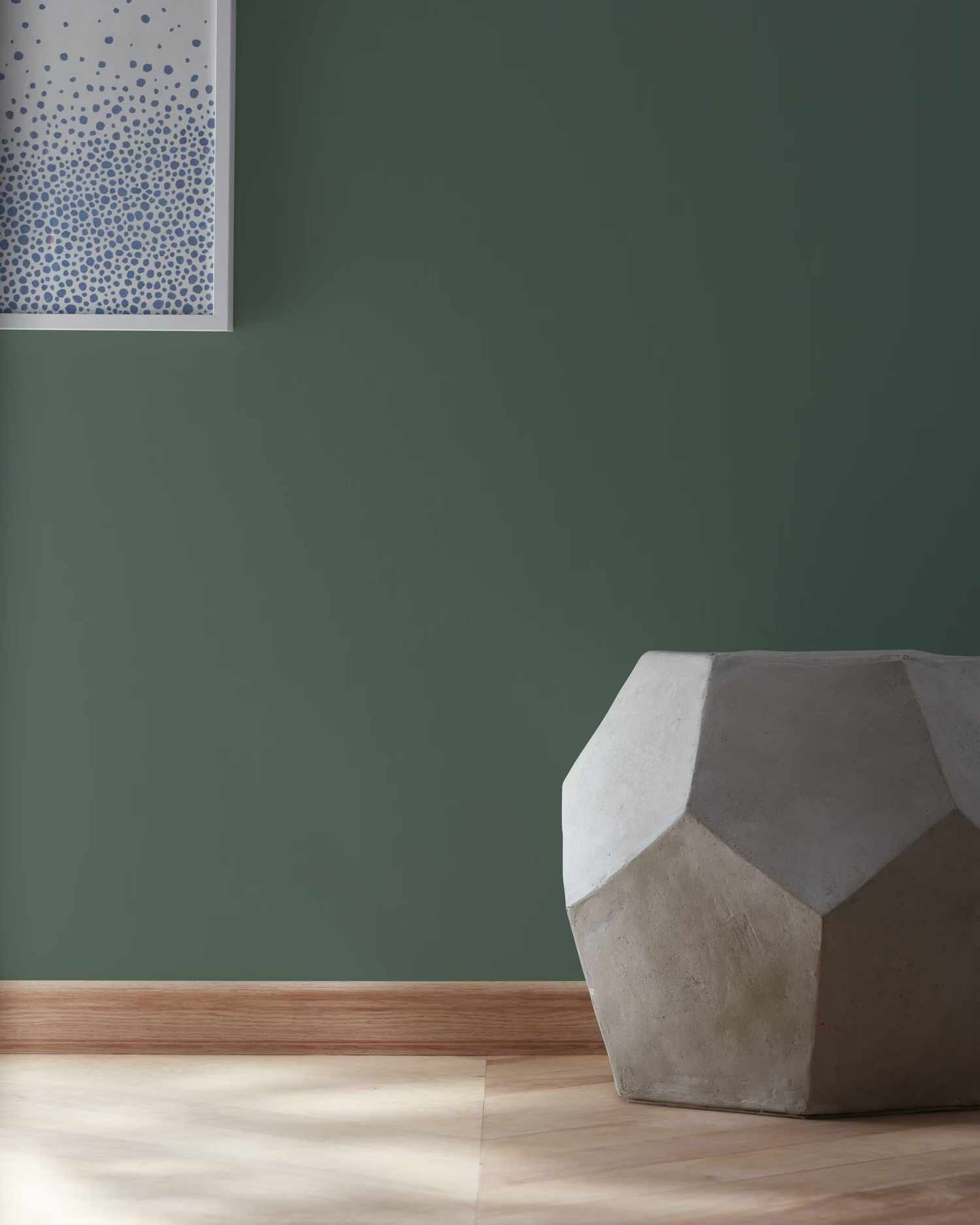 Geometric cement stool on a wooden floor against a painted wall framed art partially visible on the wall