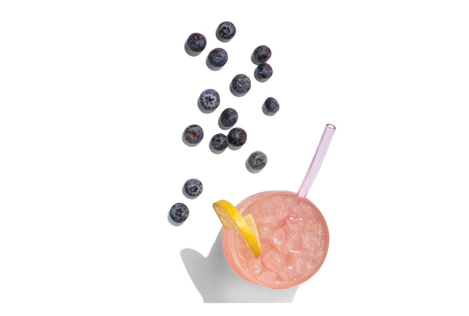 A beverage in a glass with ice lemon wedge and scattered blueberries