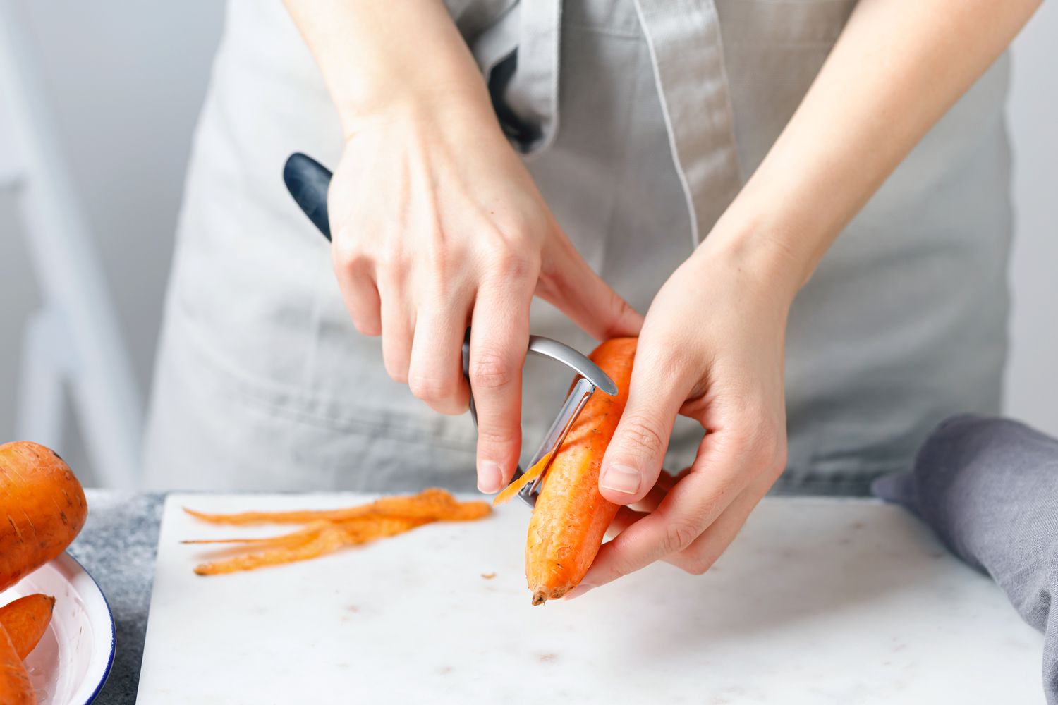 Person peeling a carrot with a hand peeler on a cutting surface