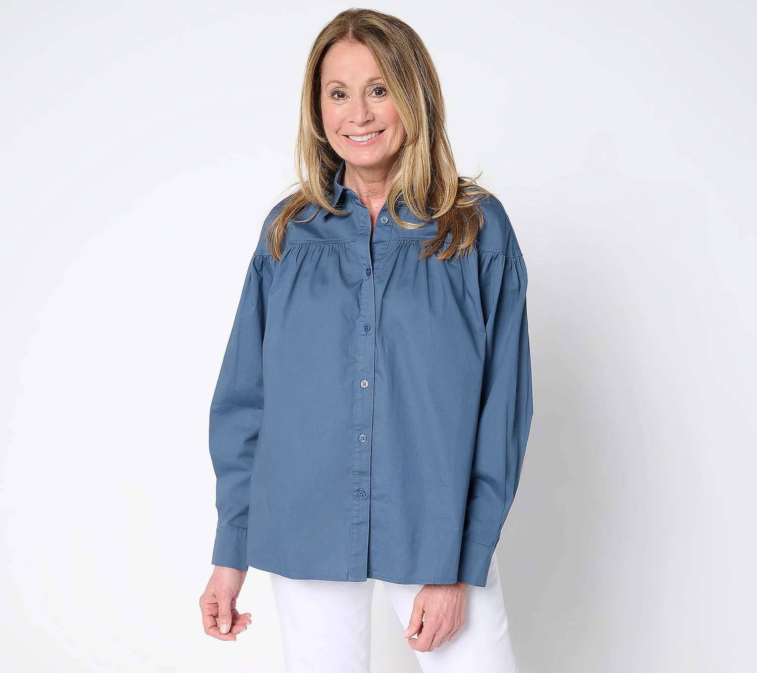 Person wearing a button-up shirt with a gathered yoke, standing and smiling. 