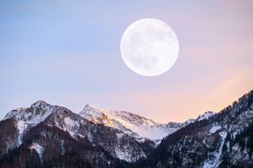 Full moon rising over snowcovered mountains with a soft gradient sky