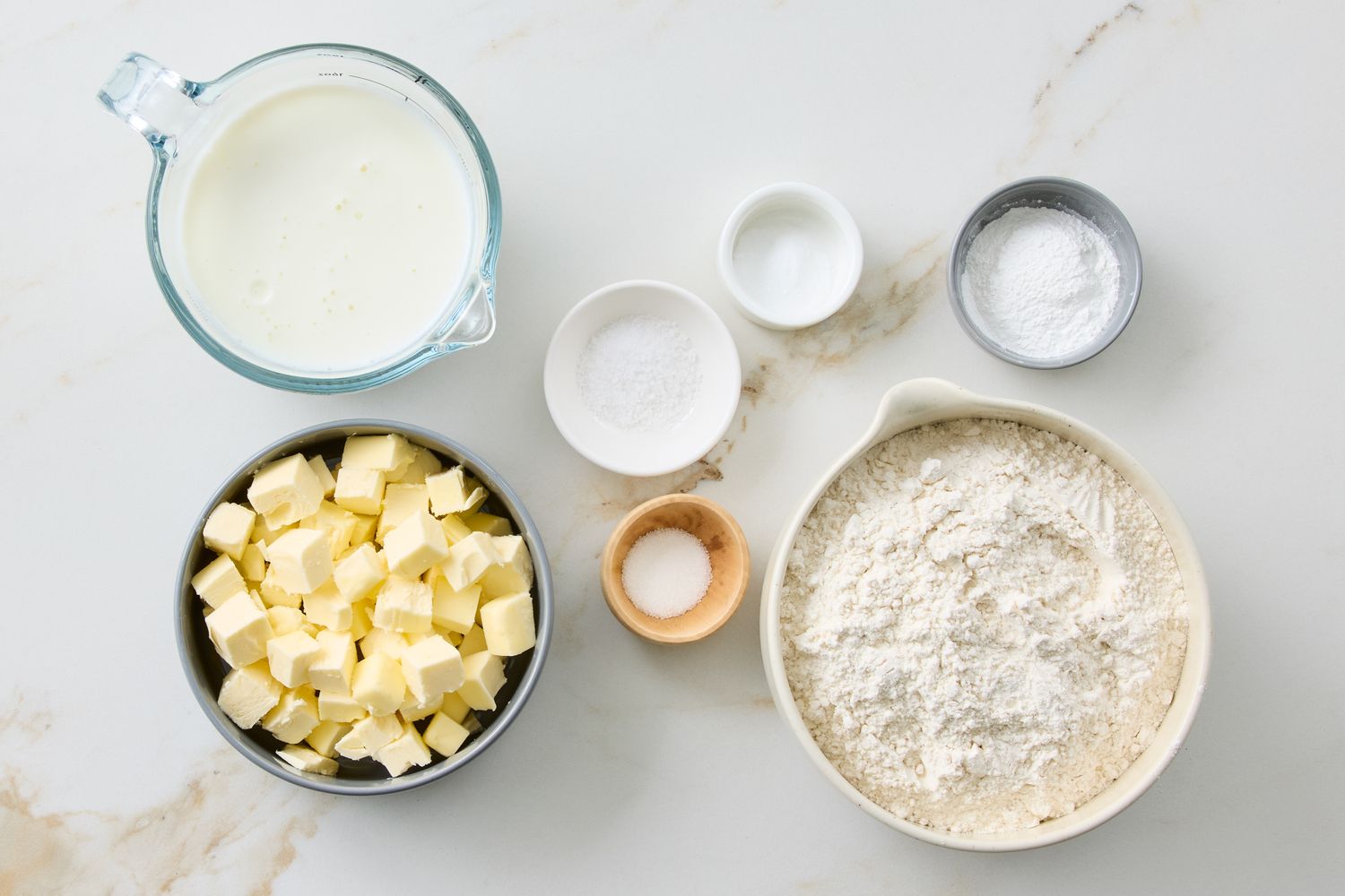 Ingredients arranged for making buttermilk biscuits including flour butter buttermilk and small bowls with other ingredients