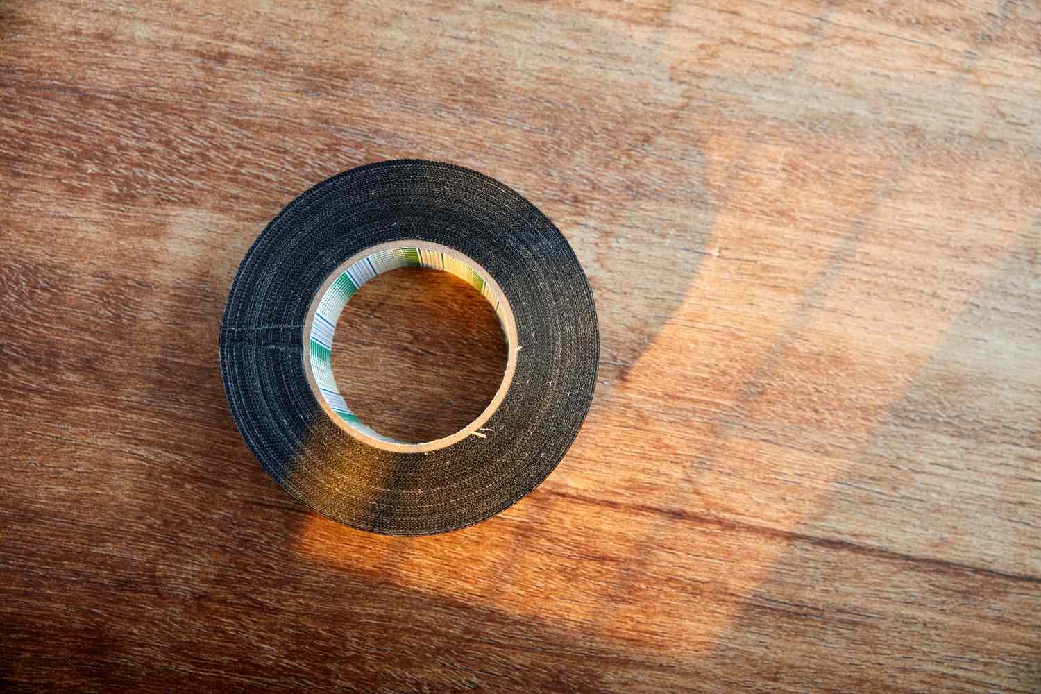 A roll of black tape resting on a wooden surface, sunlight creating shadows across the surface