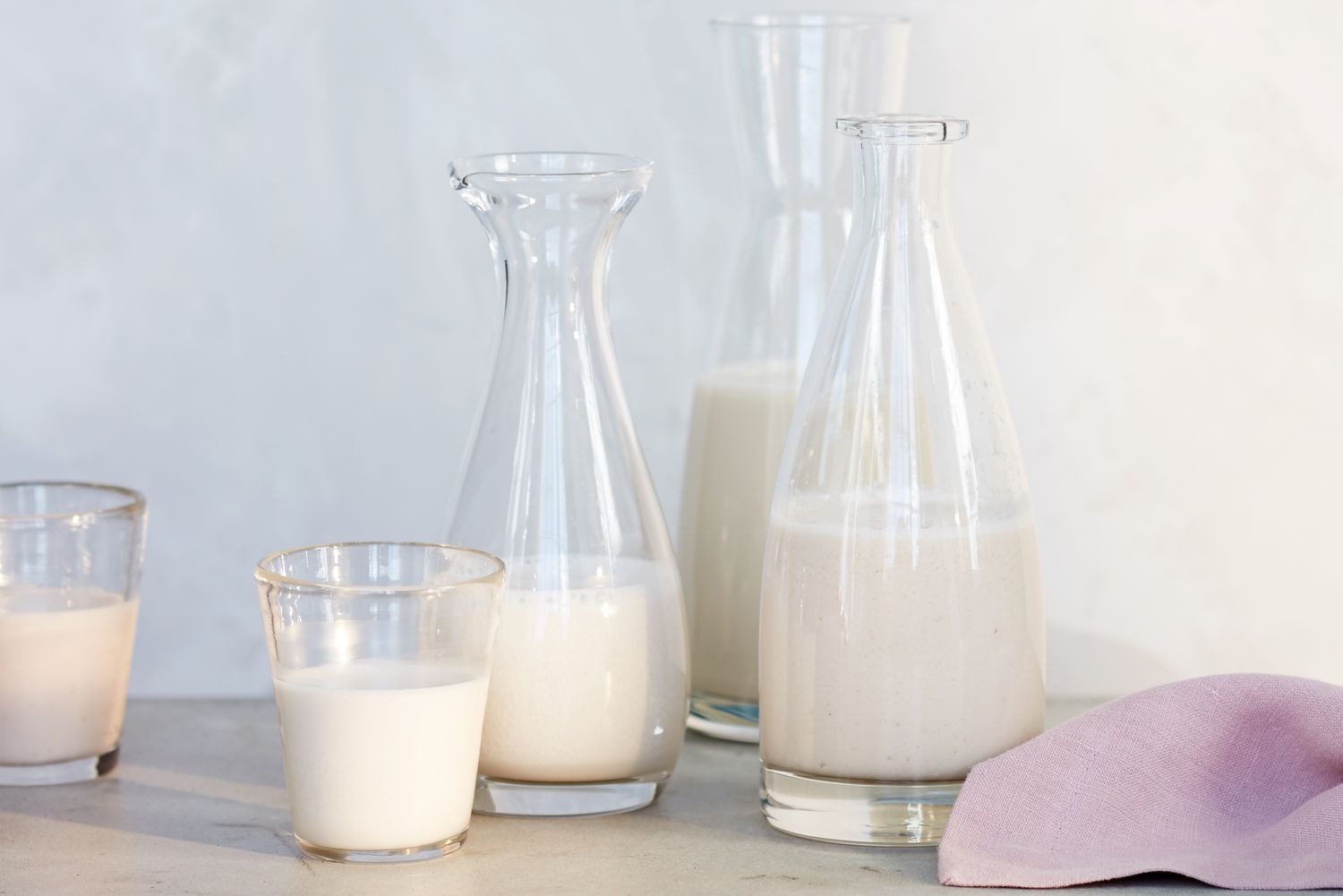 Various glass containers filled with milk arranged on a surface alongside a napkin