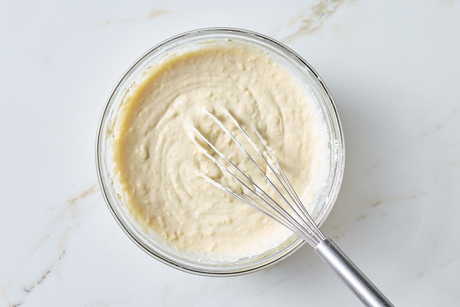 A bowl containing waffle batter with a whisk resting inside