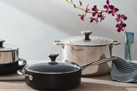 Cookware including pots and a pan displayed on a table with a striped fabric and an orchid branch in a vase