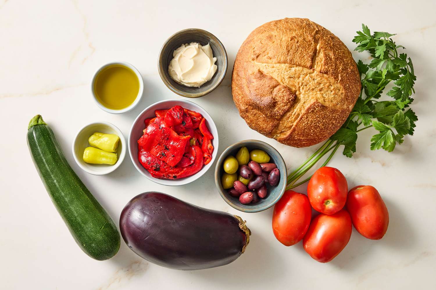 Ingredients on a kitchen counter including a loaf of bread various vegetables olives and other ingredients for preparing a dish