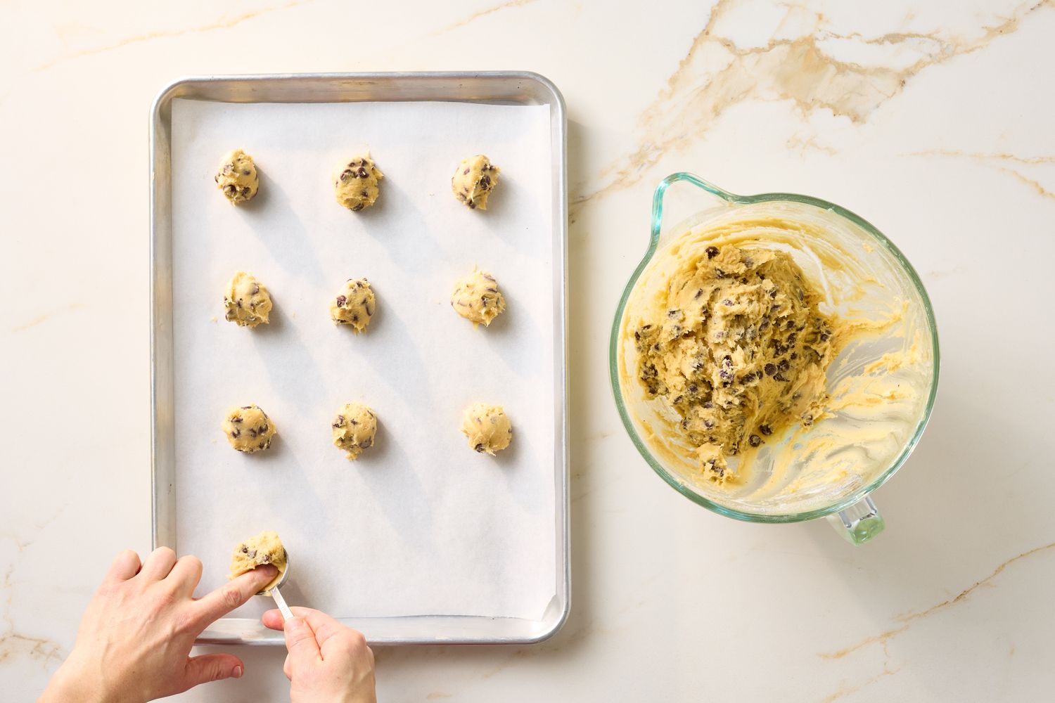 Baking preparation showing cookie dough on a parchmentlined tray and in a mixing bowl with hands shaping dough balls