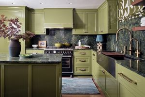 Kitchen design by Morgan Madison Design | Photography by Stephen Karlisch: glossy olive cabinetry, dramatic green marble countertops and backsplash, brass hardware, and a statement black range. A custom fluted island and patterned Roman shade add rich texture and dimension.