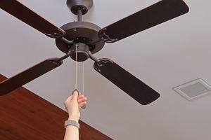 A person pulling the cord of a ceiling fan activating or adjusting its function