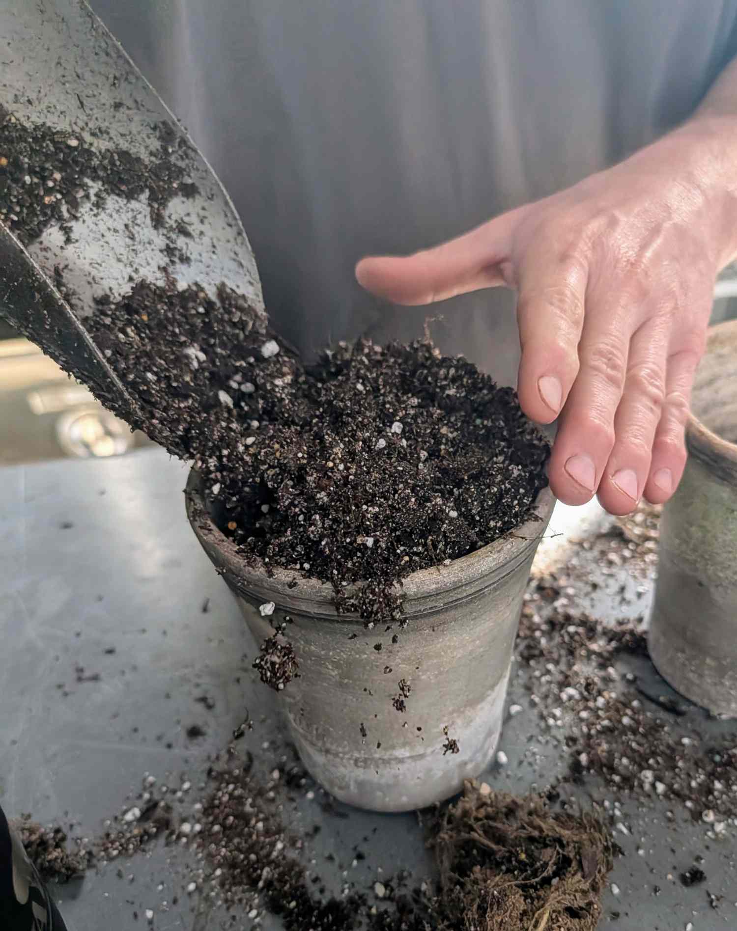 Person filling a pot with soil using a trowel hand holding the pot steady