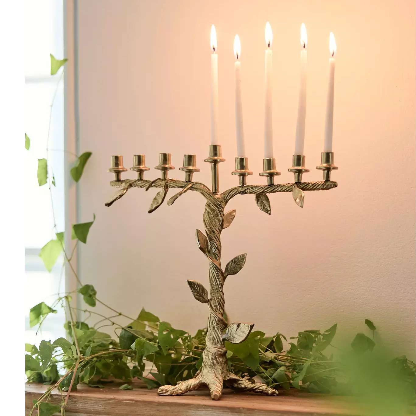 A candelabra with lit candles designed in a treelike shape displayed on a table with greenery