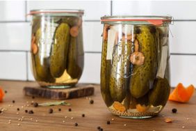 Two glass jars filled with pickles and seasonings on a wooden surface