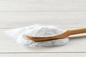 A wooden spoon resting on a pile of baking soda on a light wood surface