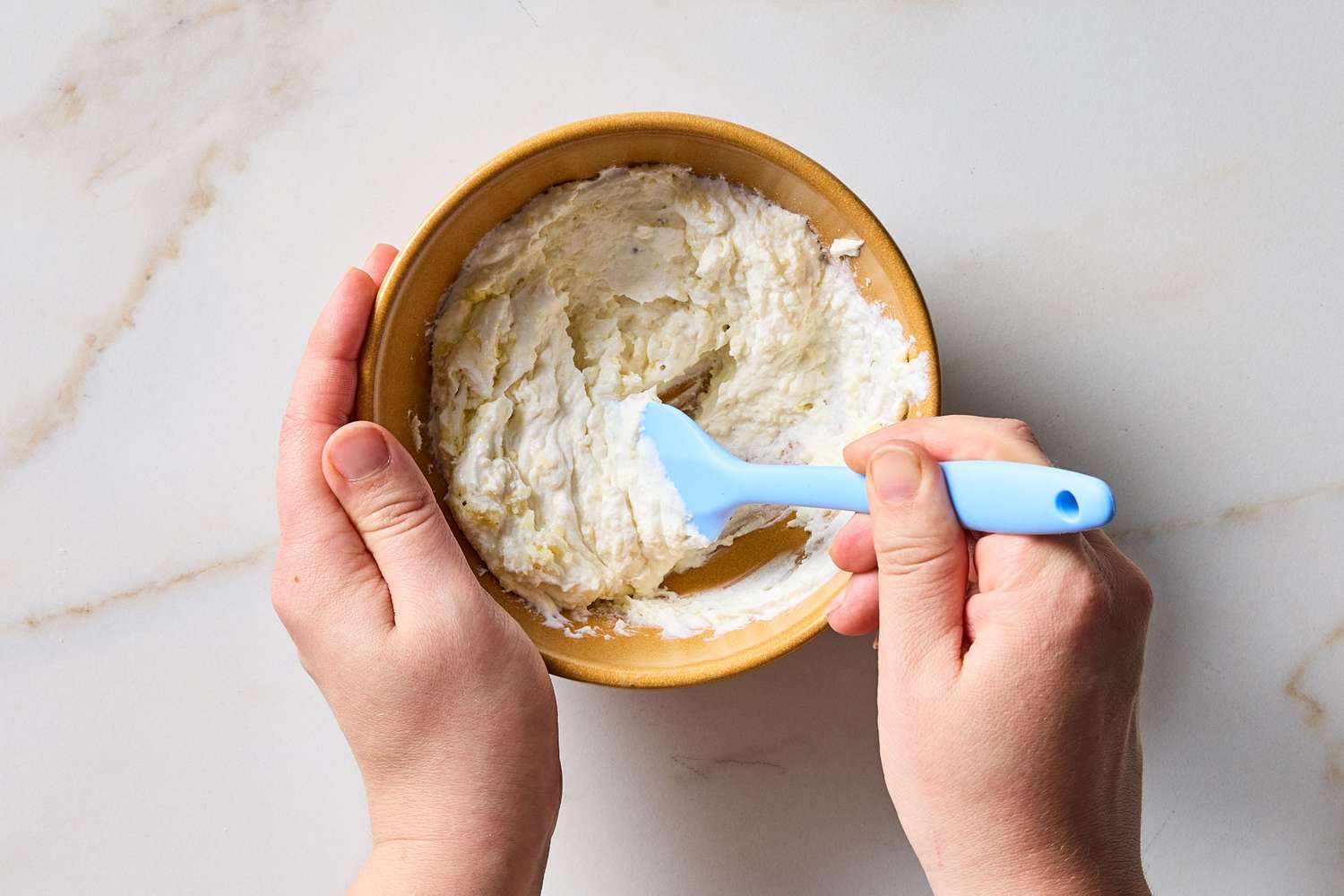 Hands mixing ricotta cheese in a bowl with a small spatula