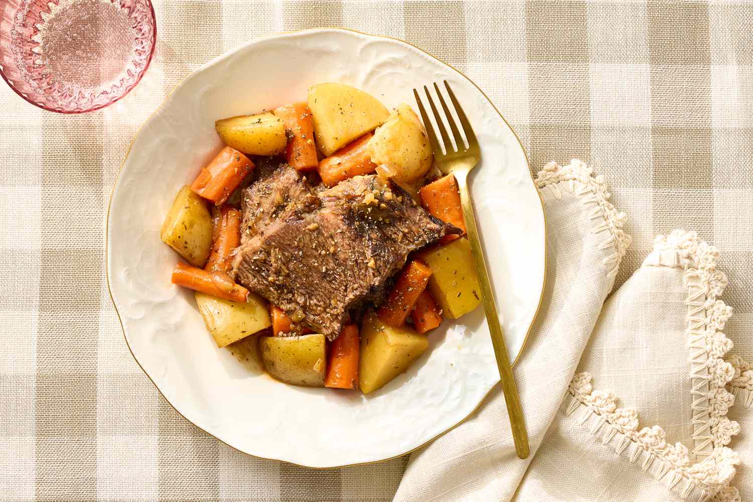 Plate with pot roast carrots and potatoes placed on a checkered tablecloth