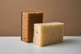 Two rectangular sponges resting on a surface one with a sponge side and a scrubbing pad side the other plain