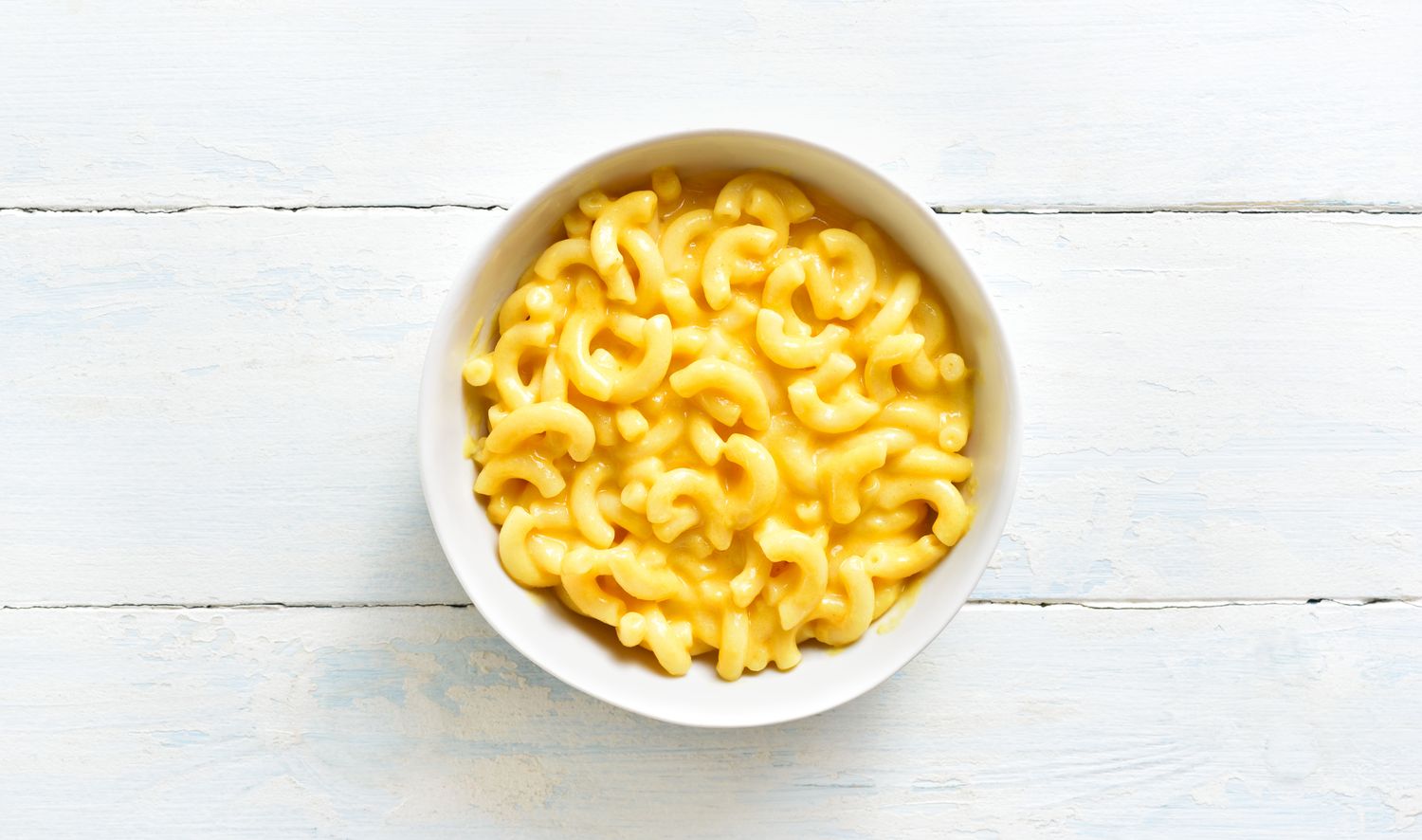 A bowl of macaroni and cheese on a wooden surface