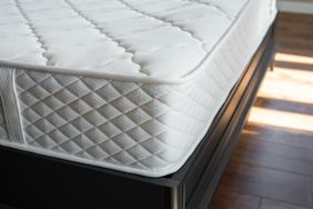 Closeup view of a mattress on a bed frame in a room with hardwood flooring