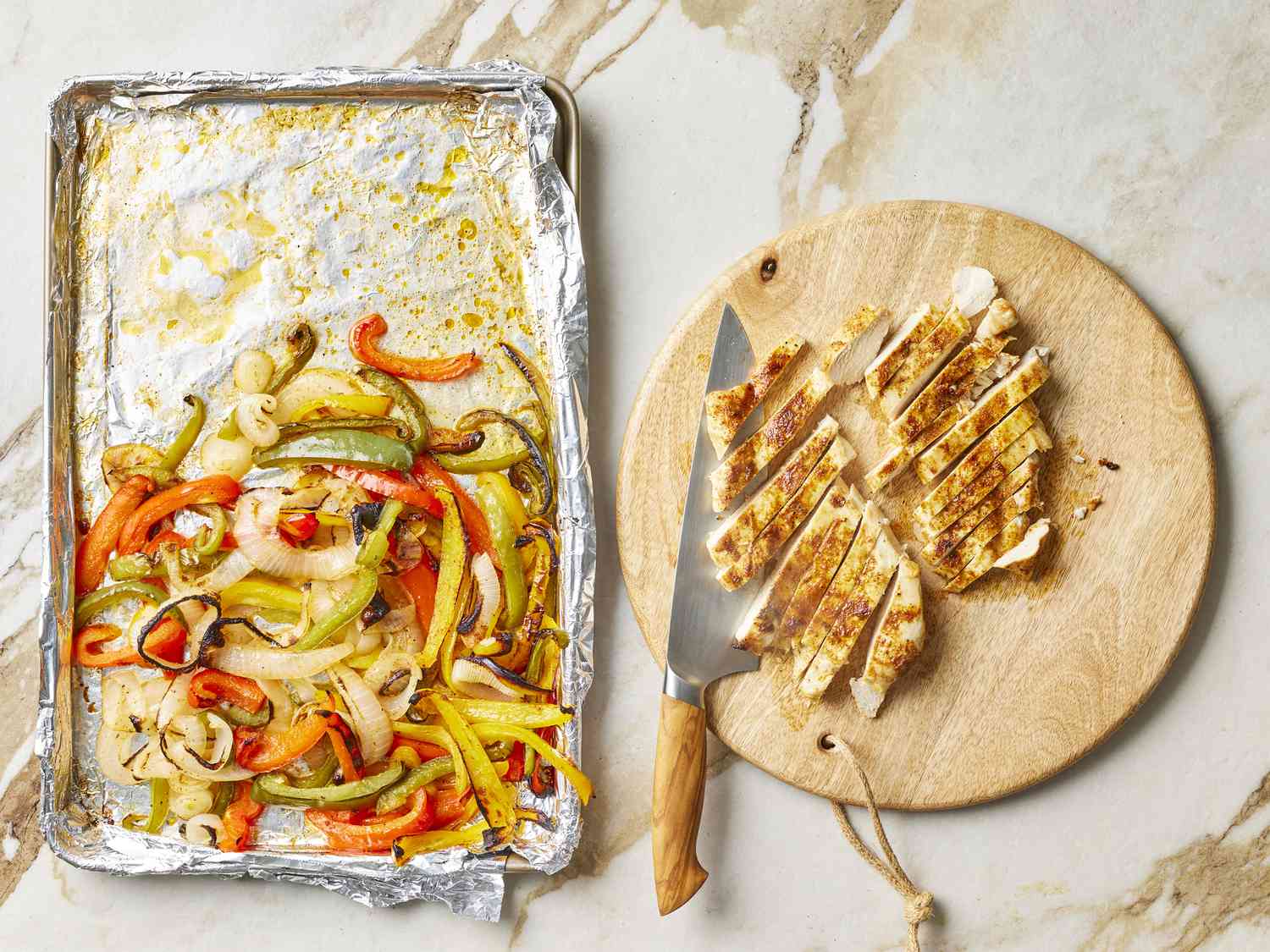 Chicken on cutting board sliced next to vegetables on sheetpan