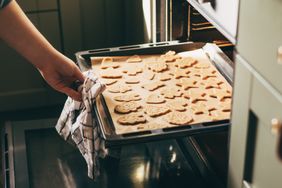 A person placing a tray of shaped cookies into an oven