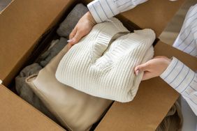 A person placing clothing items including a sweater into a cardboard box symbolizing a donation or packing activity