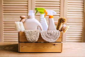 A wooden box containing various cleaning supplies including brushes scrubbers and bottles of cleaning products