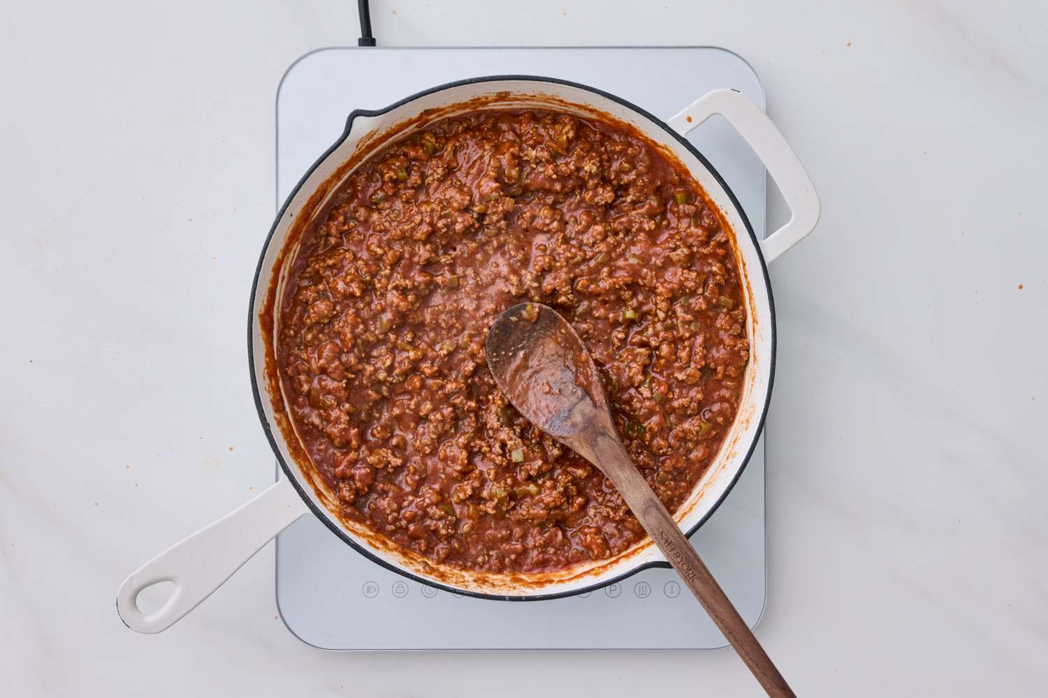 A pot of cooked sloppy joe meat with a wooden spoon on a stovetop