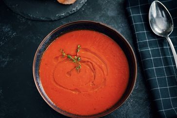 A bowl of tomato soup garnished with herbs placed beside a black napkin and spoon