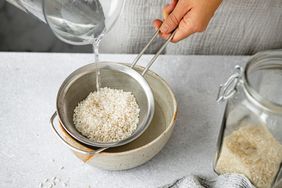 Hand rinsing uncooked rice in a metal sieve with a jar of rice on the side