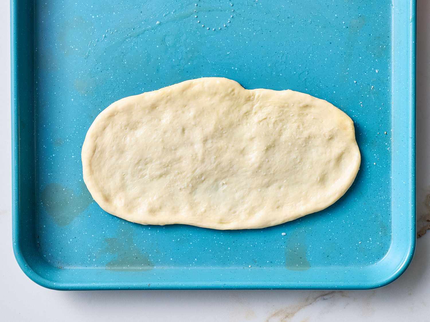 Pizza dough shaped into an oval on a blue baking tray, ready for topping before baking