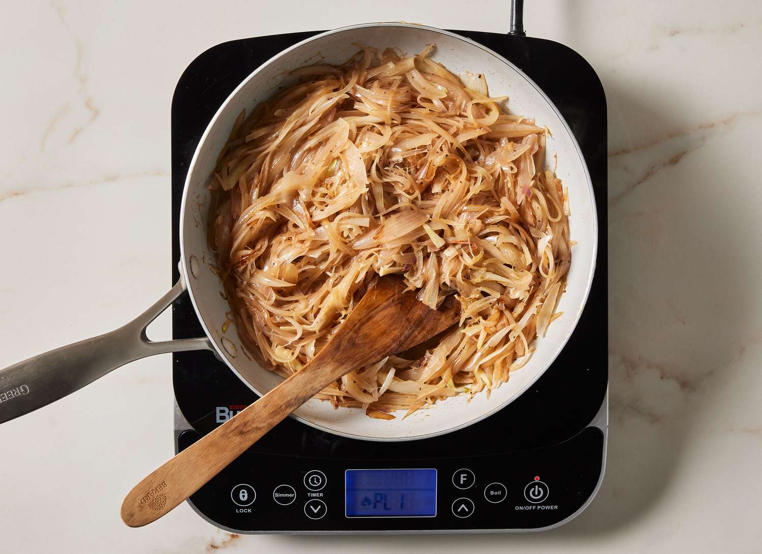 caramelized sliced shallots in a pan with a wooden spoon