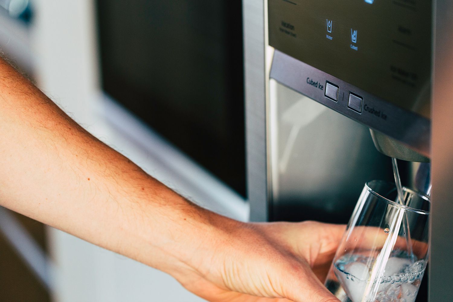 Person holding a glass up to water dispenser in fridge