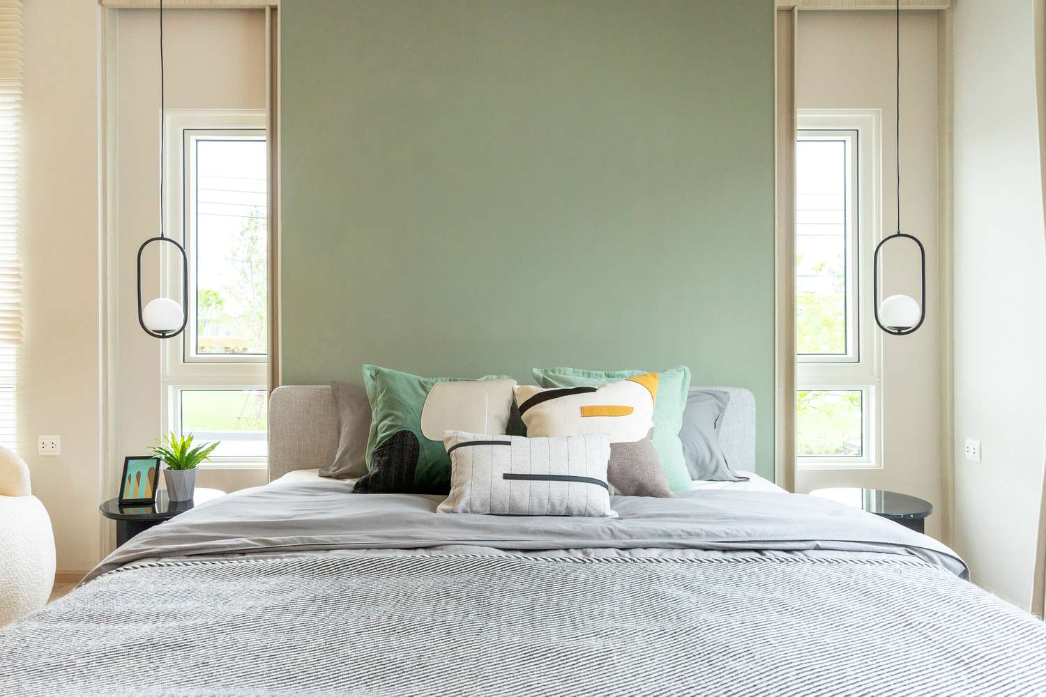Stylish bedroom with green accent wall two windows pendant lights and a wellorganized bed with decorative pillows