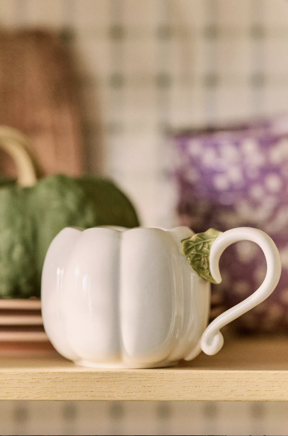 Pumpkinshaped ceramic mug with a handle featured on a wooden shelf
