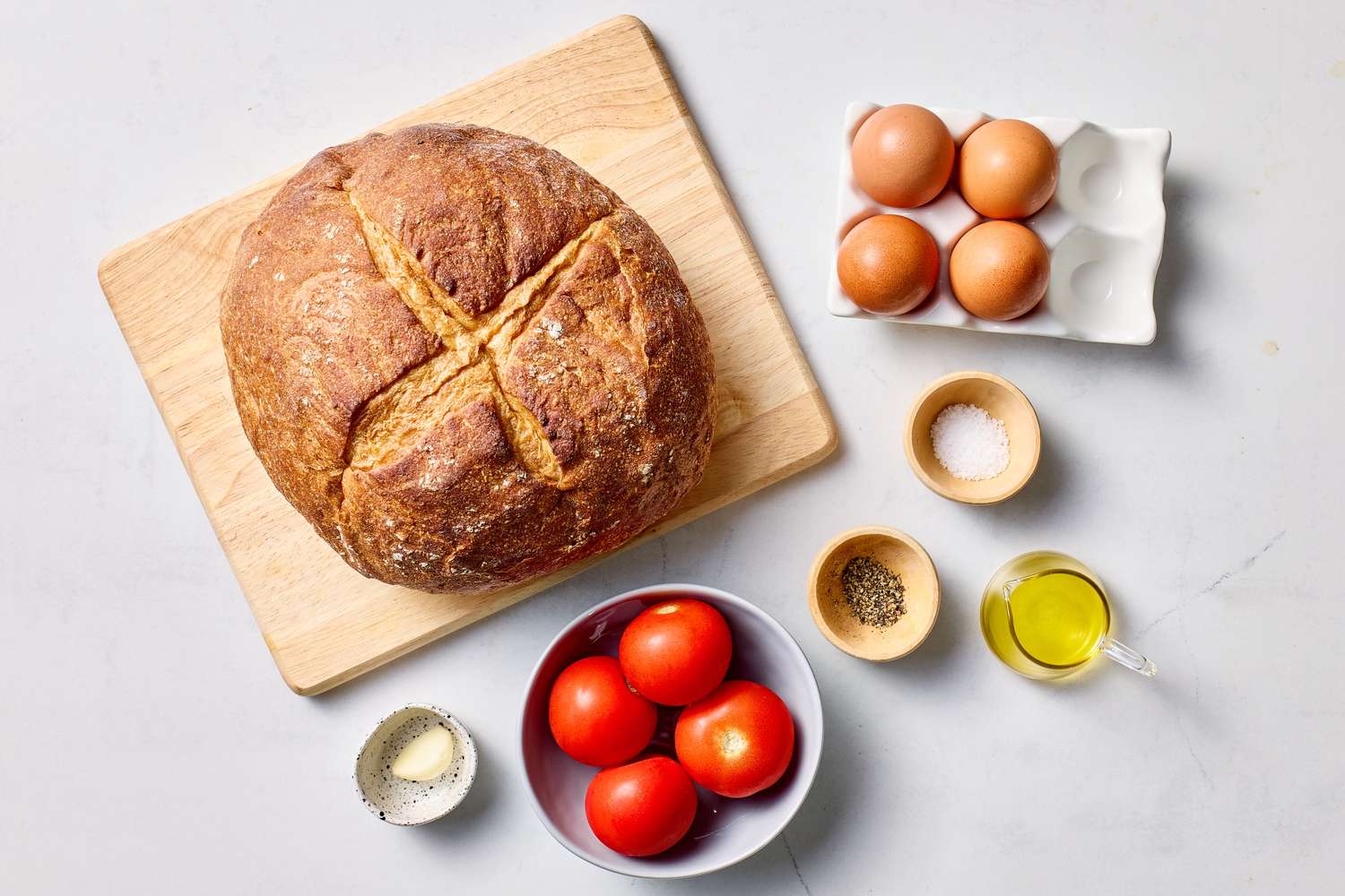 Ingredients for a recipe including bread eggs tomatoes spices oil and other items arranged on a surface
