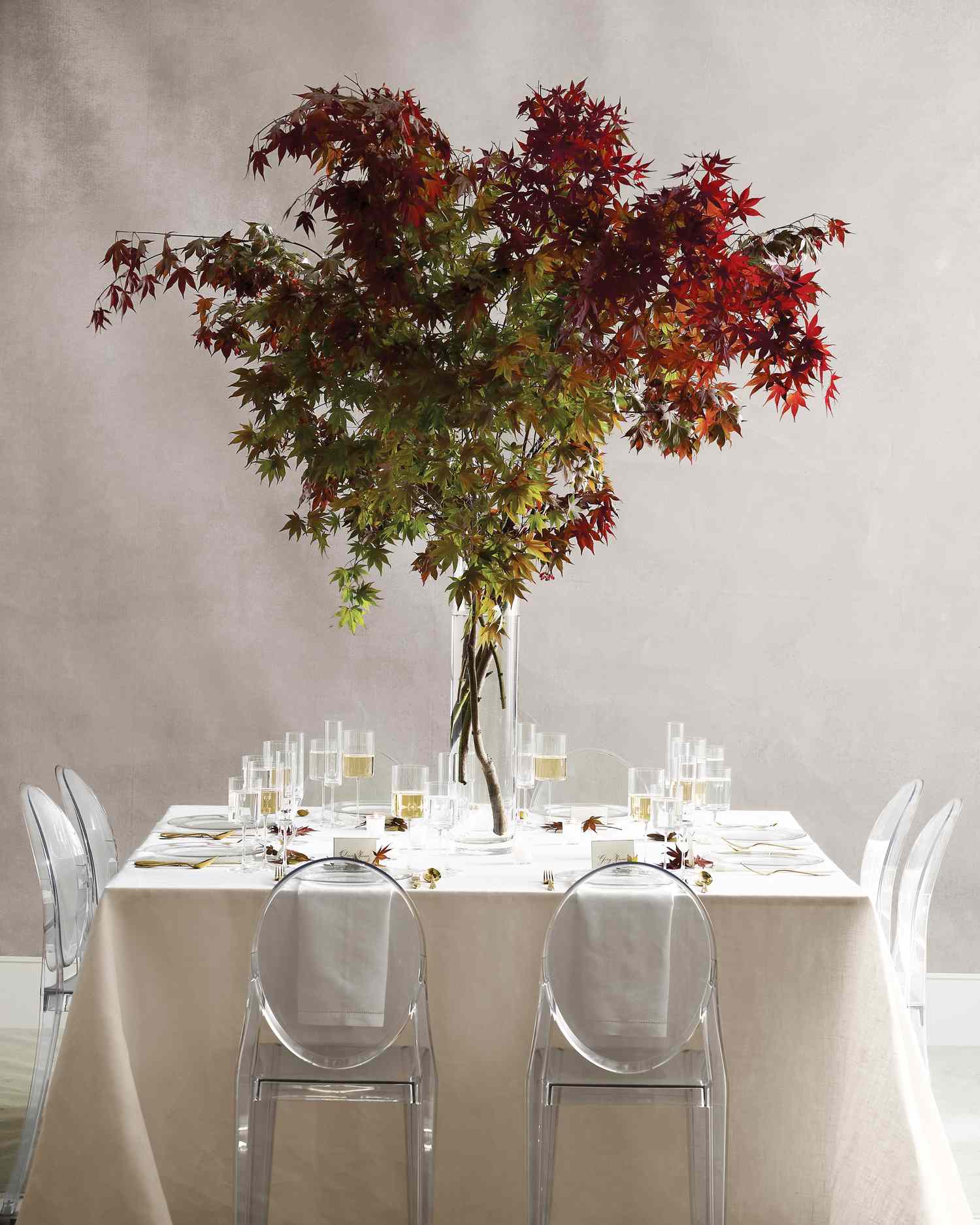 Table with a large centerpiece made of maple branches in a tall vase