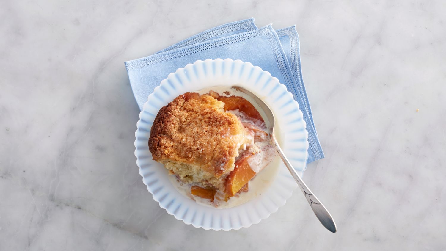 portion of peach cobbler in small bowl with cream and spoon