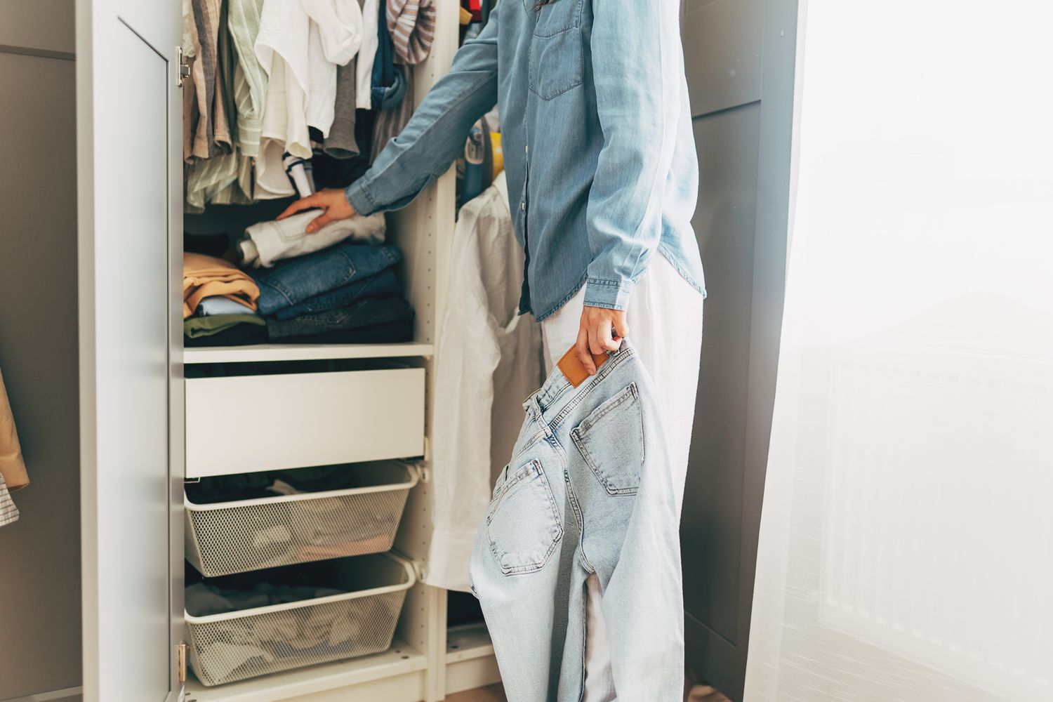 A person organizing clothes in a closet holding a pair of jeans in one hand