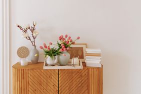 A wooden sideboard with decorative vases flowers books and framed art