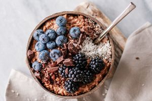 A bowl of oatmeal topped with blueberries blackberries shredded coconut and chocolate chunks on a table with a napkin